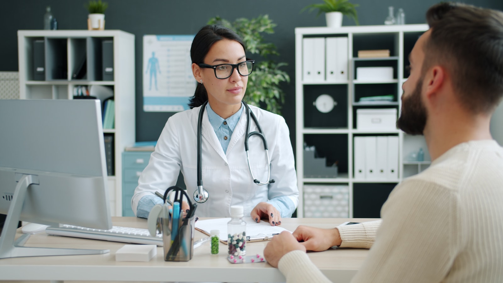 A doctor talking a patient through a treatment plan across a consulting-room desk.